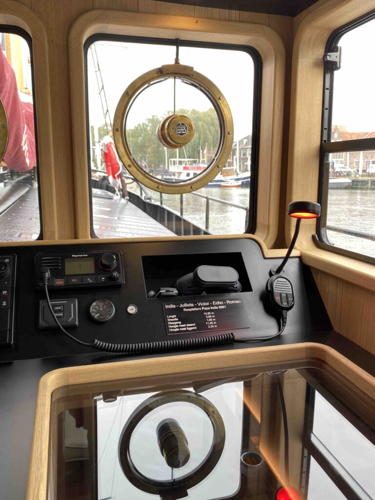 De stuurstand met houten stuurwiel, navigatieapparatuur en uitzicht rondom.