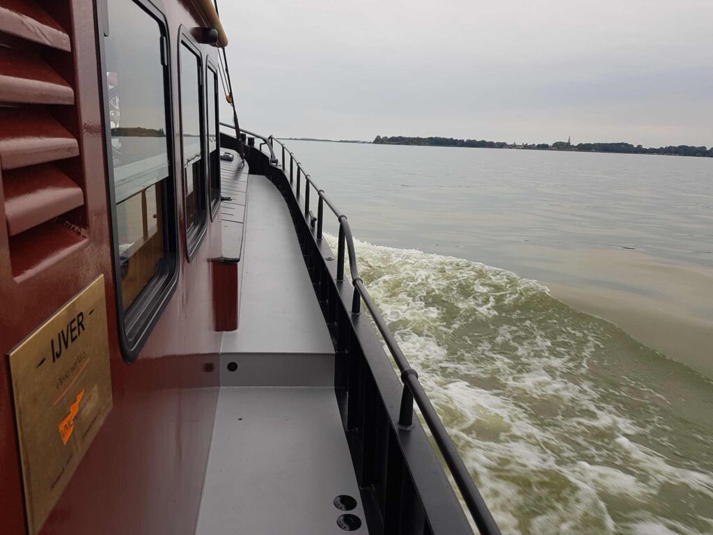 Uitzicht langs het gangboord tijdens het varen, met het water vlak naast het schip.