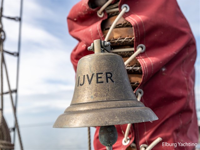 De scheepsbel met de naam IJver, opgehangen bij de mast.