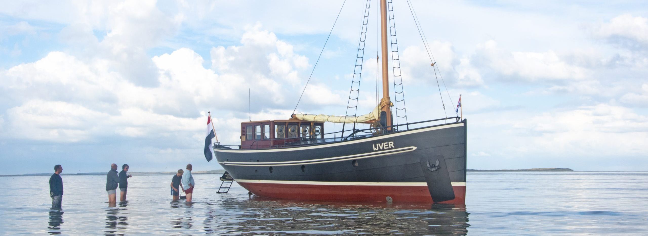 Wandelen naast De IJver bij laagwater, met het drooggevallen schip midden in het weidse Wad.